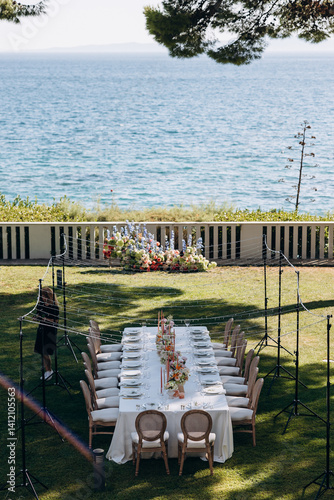 wedding. A festive table adorned with flowers and candles stands on a green meadow among the trees, with a view of the sea and the sky