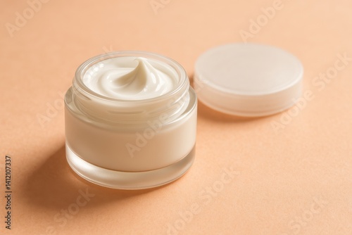 Cream in Clear Container on Peach Surface Highlighting Beauty Products Textur...
