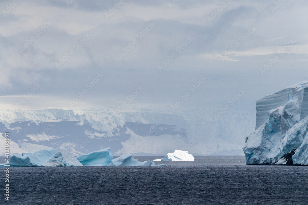A tranquil Antarctic landscape, near Graham passage along Charlotte Bay, highlighting stark reflections, rugged mountains, and impressive icebergs.