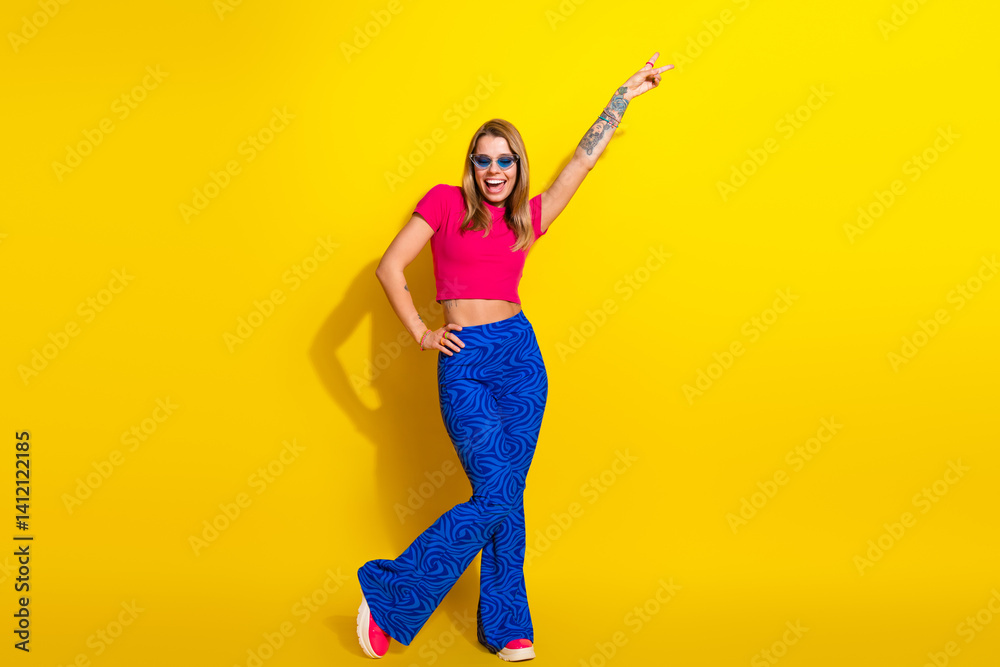 Cheerful young woman in colorful modern fashion posing against vibrant yellow background Cheerful young woman in colorful modern fashion posing against vibrant yellow background
