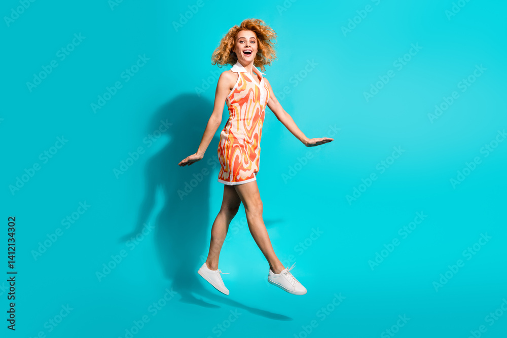 Joyful young woman in a vibrant patterned dress, jumping playfully against a bright turquoise background Joyful young woman in a vibrant patterned dress, jumping playfully against a bright turquoise background