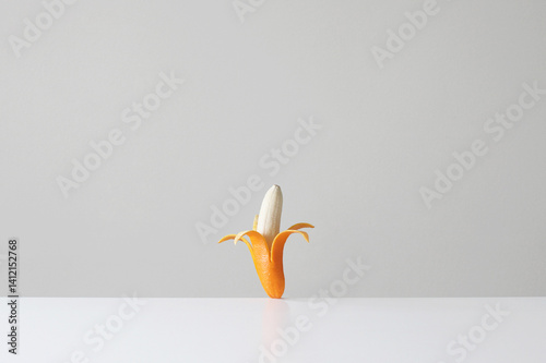 Conceptual genetically modified banana in an orange skin on a table in front of a white background 