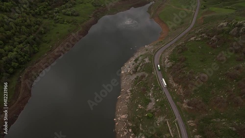 Aerial view of a snake-like road lined with rolling hills and a lake, with vehicles moving along photo