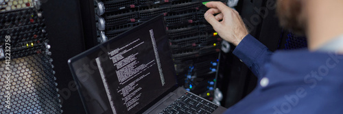Website header shot of technician working with laptop connected to computer server, managing server rack with detailed interface and various indicator lights in background