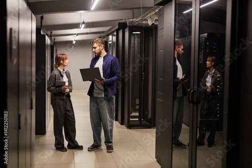 Wallpaper Mural Two IT professionals discussing data management in a modern server room with servers visible through glass doors. Man holding laptop and showing woman data on screen Torontodigital.ca