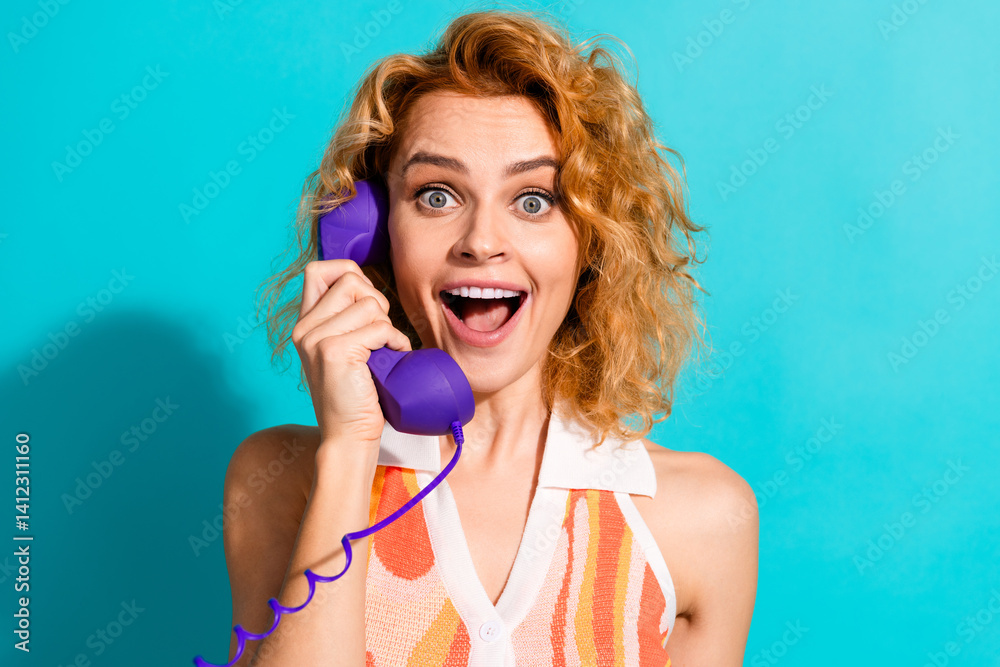 Naklejka premium Cheerful Young Woman With Red Hair Smiling Excitedly While Talking on a Retro Purple Phone Against a Vibrant Teal Background