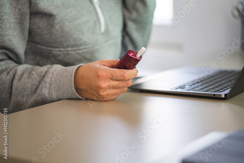 unknown woman work on laptop and use electronic cigarette at office