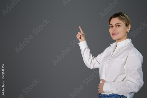 A blonde girl near a gray wall points to the space with her finger. Teacher in white office shirt pointing to empty space for copy and text, pile paste, woman smiling, whiteboard