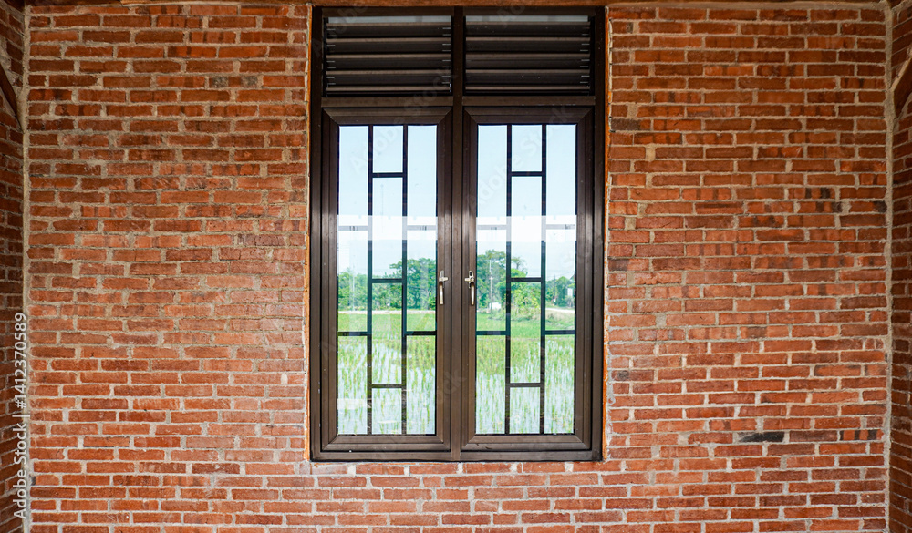 Fototapeta premium A window with metal bars set against a brick wall, offering a glimpse of the outside landscape through the glass. The image captures a rustic architectural feature.