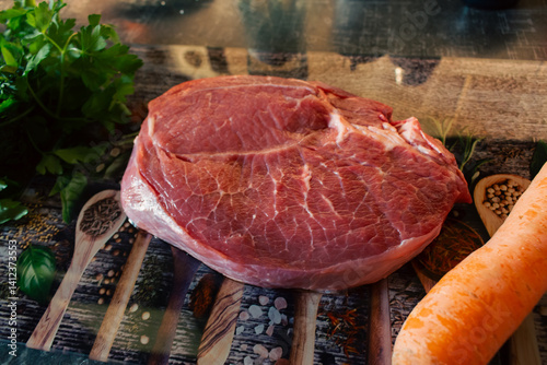 Obraz na płótnie Raw beaf steak with carrot and parsley on cutting board. Raw meat, herbs and vegetable on table. Kitchen interior. Steak preparation process. Food styling. Marble steak on cutting board. w salonie