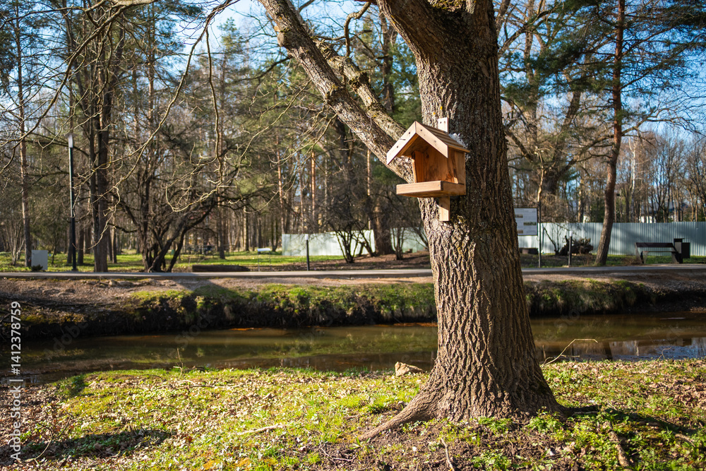 A charming birdhouse is hung from a tree branch, set against the backdrop of a serene river or stream and lush forest.