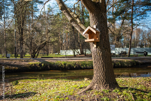 Obraz na płótnie A charming birdhouse is hung from a tree branch, set against the backdrop of a serene river or stream and lush forest. w salonie