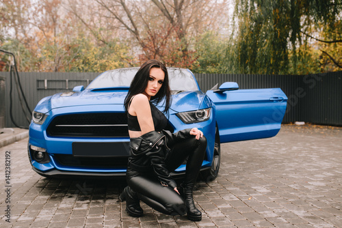 Stylish woman in black outfit posing with blue sports car