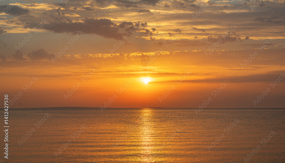 A breathtaking sunset casts golden hues across a calm sea, painting the sky with warm tones and tranquil beauty.