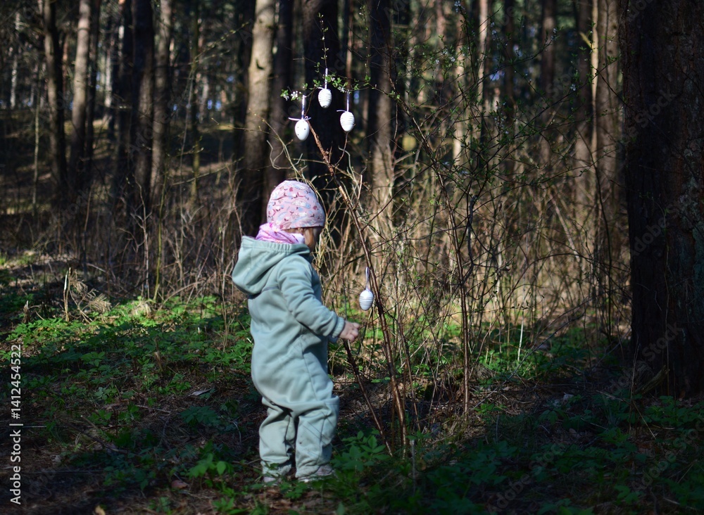 Toddler girl hanging easter eggs decorations on the bush in the forest. Baby girl playing with easter egg decorations in the park. Concept of kid preparing for easter holidays. Toddler girl hanging easter eggs decorations on the bush in the forest. Baby girl playing with easter egg decorations in the park. Concept of kid preparing for easter holidays.