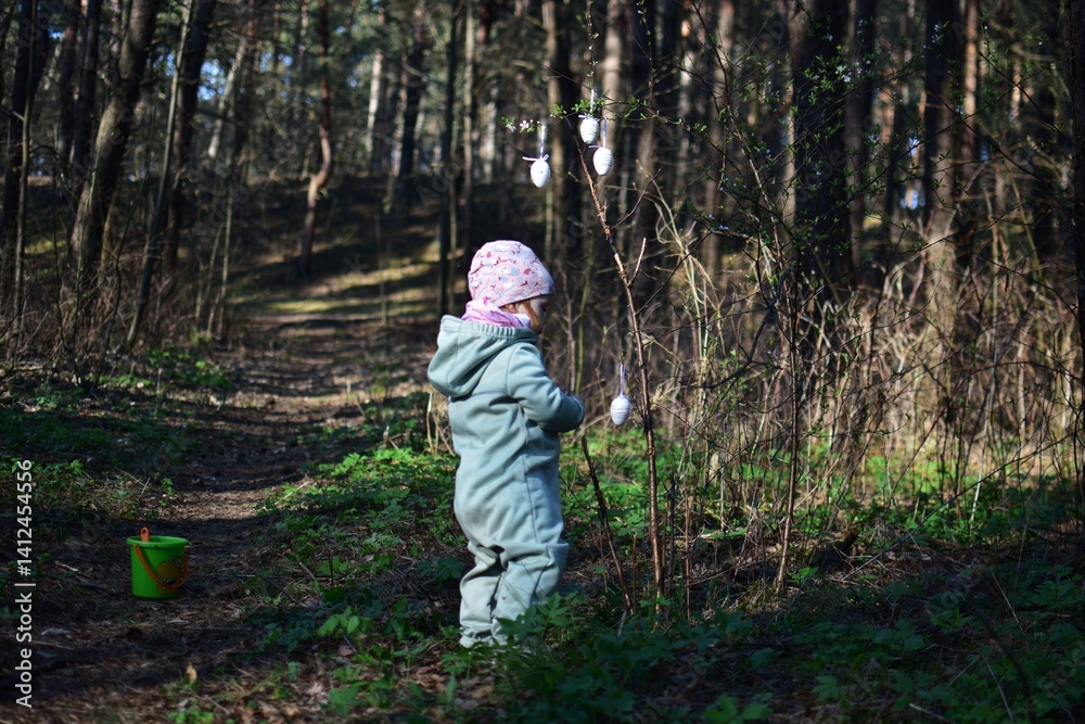 Toddler girl hanging easter eggs decorations on the bush in the forest. Baby girl playing with easter egg decorations in the park. Concept of kid preparing for easter holidays. Toddler girl hanging easter eggs decorations on the bush in the forest. Baby girl playing with easter egg decorations in the park. Concept of kid preparing for easter holidays.