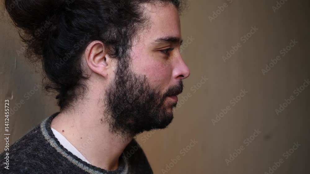 side shot of young bearded man, who looks serious and deep in thought, reflecting on something important, with a calm and contemplative expression.