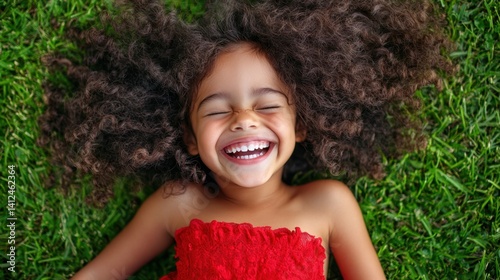 Joyful Girl in the Grass: A close-up shot of an adorable girl lies happily on the green grass, eyes closed and teeth bared, surrounded by the luxurious tangle of curly hair.