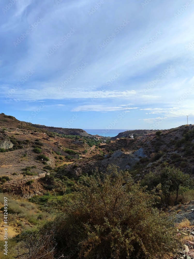 Landscape view of hills and coastline under a blue sky with scattered clouds Landscape view of hills and coastline under a blue sky with scattered clouds