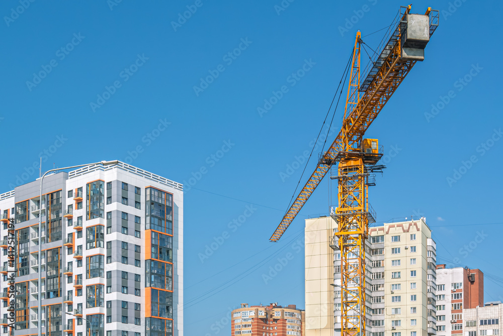 Naklejka premium Equipment for the construction and lifting of bulky goods with construction materials. A tower crane next to new buildings. Construction equipment. Engineering equipment.