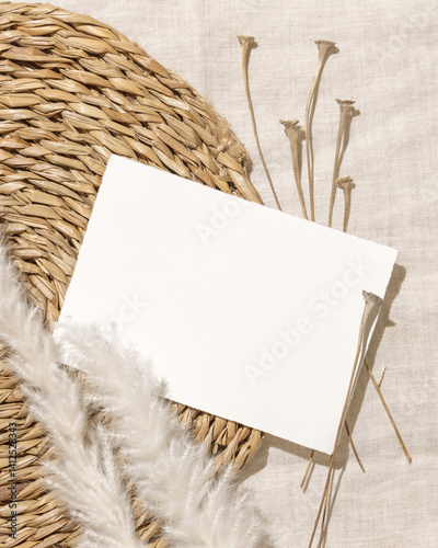 Blank card near dryed grass on beige vowen placemat and linen top view, bohemian mockup