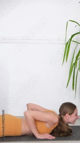 A woman in an orange tracksuit exercises on a yoga mat. On a white background, fitness and muscle building. Stretching, Pilates, and health exercises. High quality FullHD footage