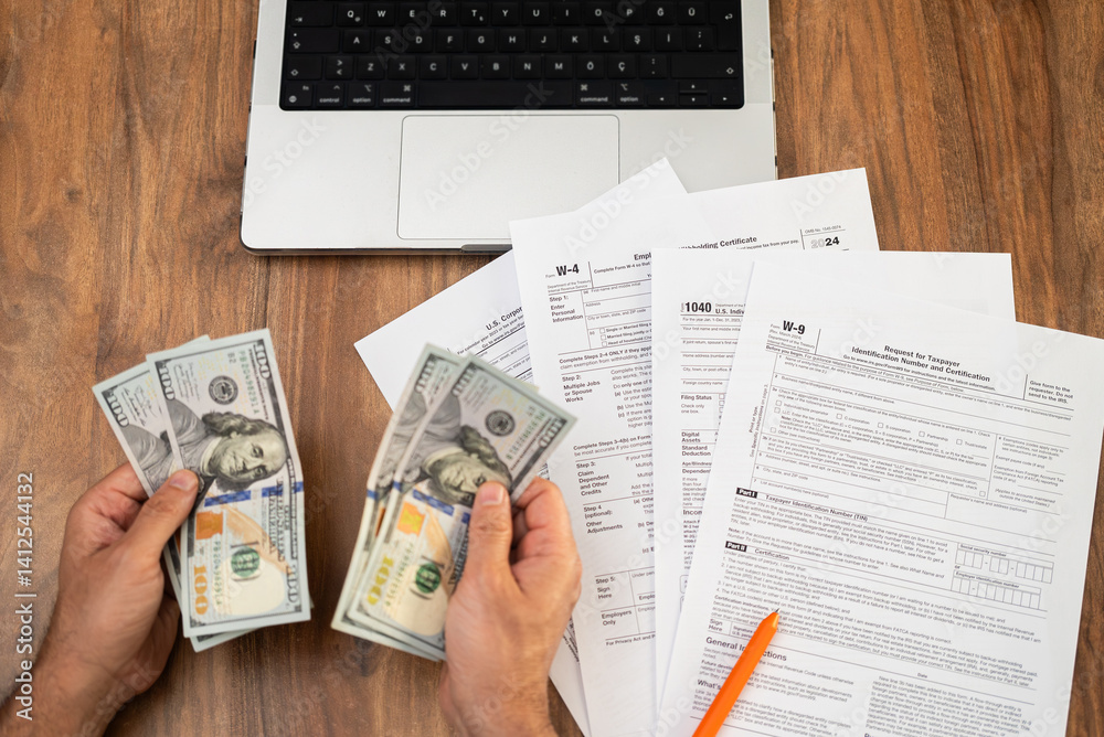 Obraz premium Male entrepreneur holds dollar banknotes in hands counting cash for filling different tax forms in accordance with strict requirements sitting at workplace with laptop