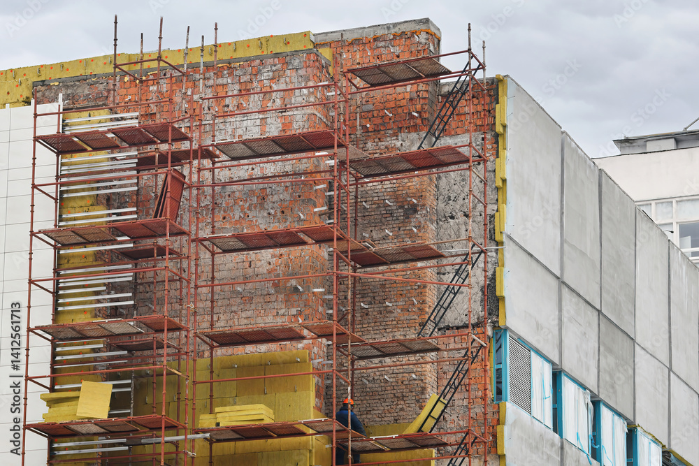 Building under exterior repair, scaffolding setup, installation of thermal insulation in urban redevelopment zone. Restoring old building facade with new thermal insulation materials, facade cladding