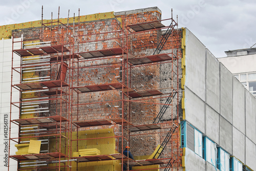 Obraz na płótnie Building under exterior repair, scaffolding setup, installation of thermal insulation in urban redevelopment zone. Restoring old building facade with new thermal insulation materials, facade cladding w salonie