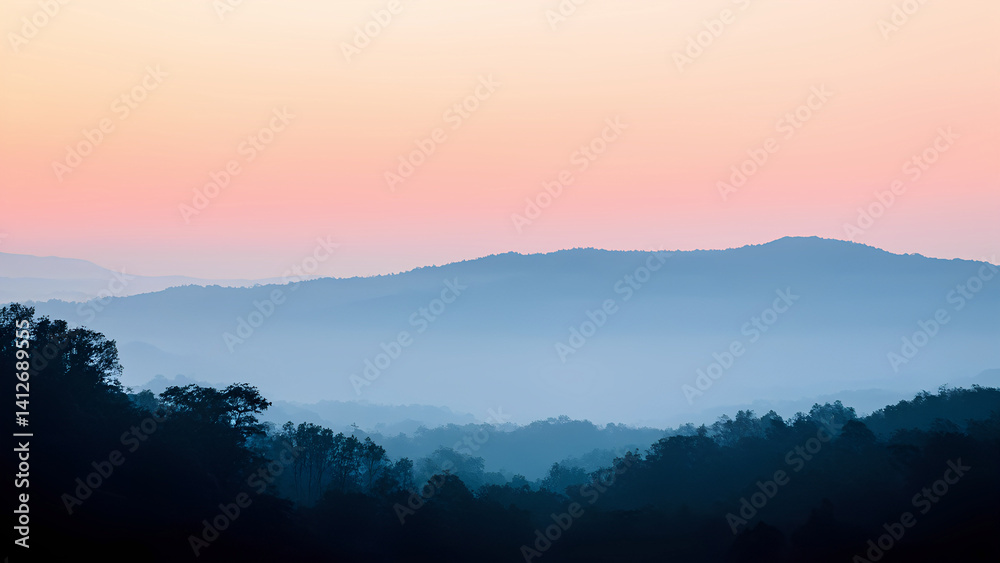 Fototapeta premium Fog-covered mountain ranges layered in distance, silhouetted trees and soft pastel sky in the background