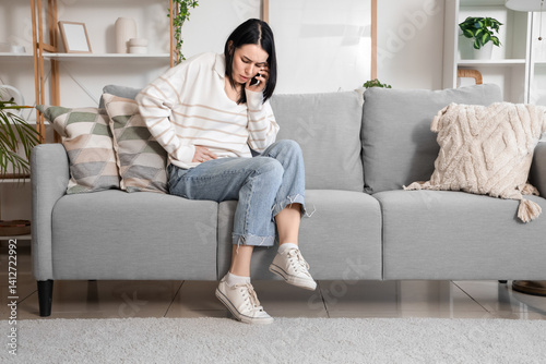 Young woman with severe abdominal pain calling an ambulance at home