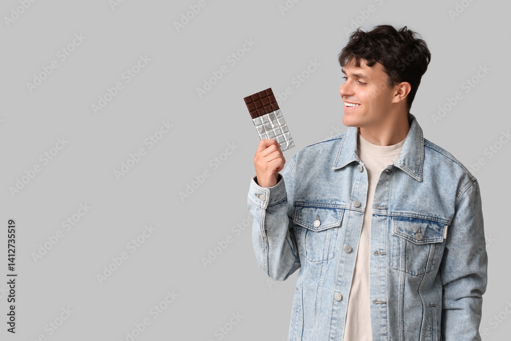Handsome young man with sweet chocolate bar on grey background Handsome young man with sweet chocolate bar on grey background
