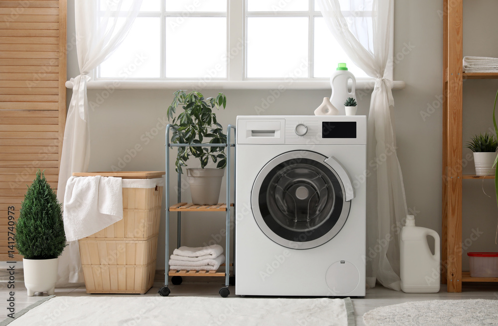 Washing machine, basket with laundry and houseplants near window in room