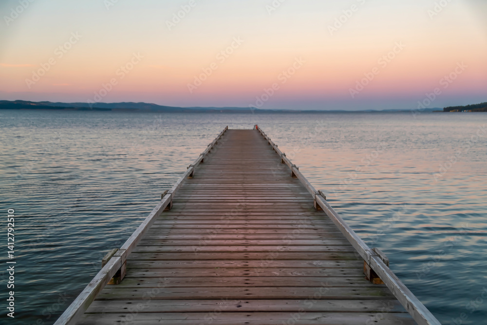 Fototapeta premium Empty wooden pier stretching into a calm lake at dusk, pastel pink and orange sky, tranquil scenery
