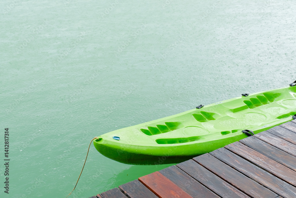 green kayak is tied to wooden dock on calm, rainy day, creating serene and peaceful scene