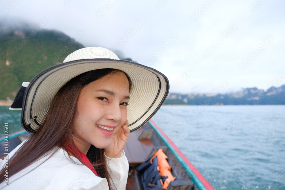 Young woman smiling on boat ride, wearing wide brimmed hat, with scenic mountains and water in background