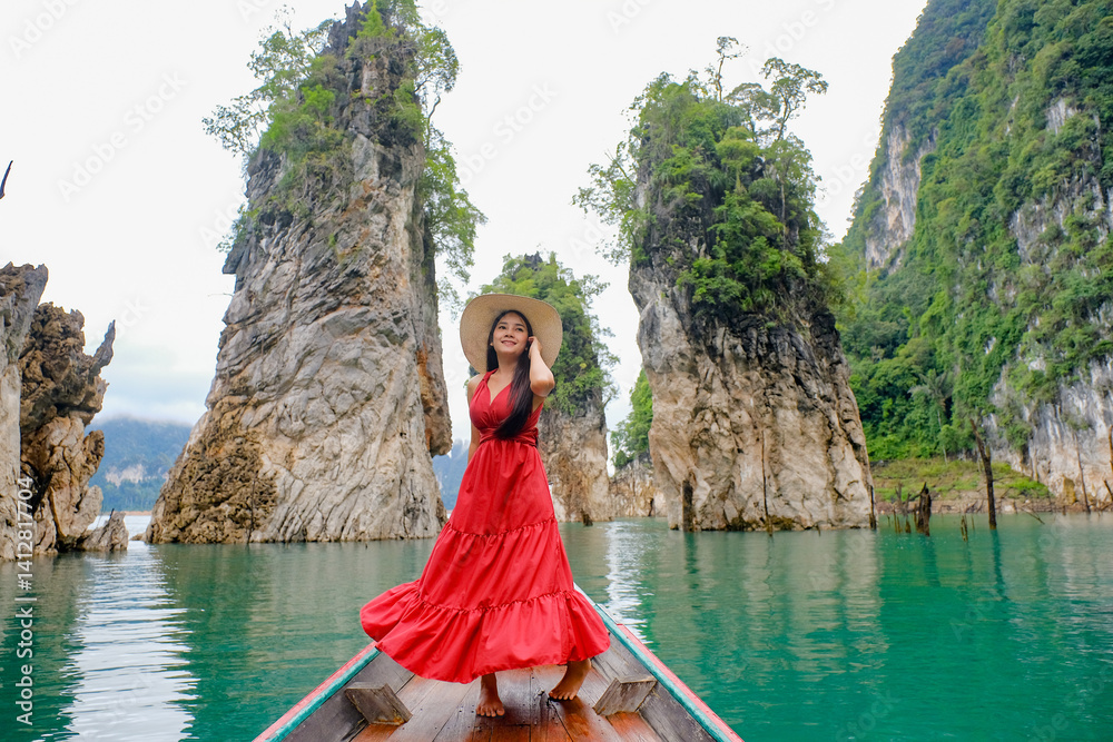 woman in red dress and hat joyfully poses on boat surrounded by stunning limestone cliffs and turquoise water