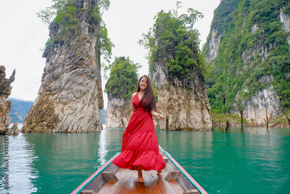 woman in red dress joyfully stands on boat surrounded by stunning limestone cliffs and turquoise water