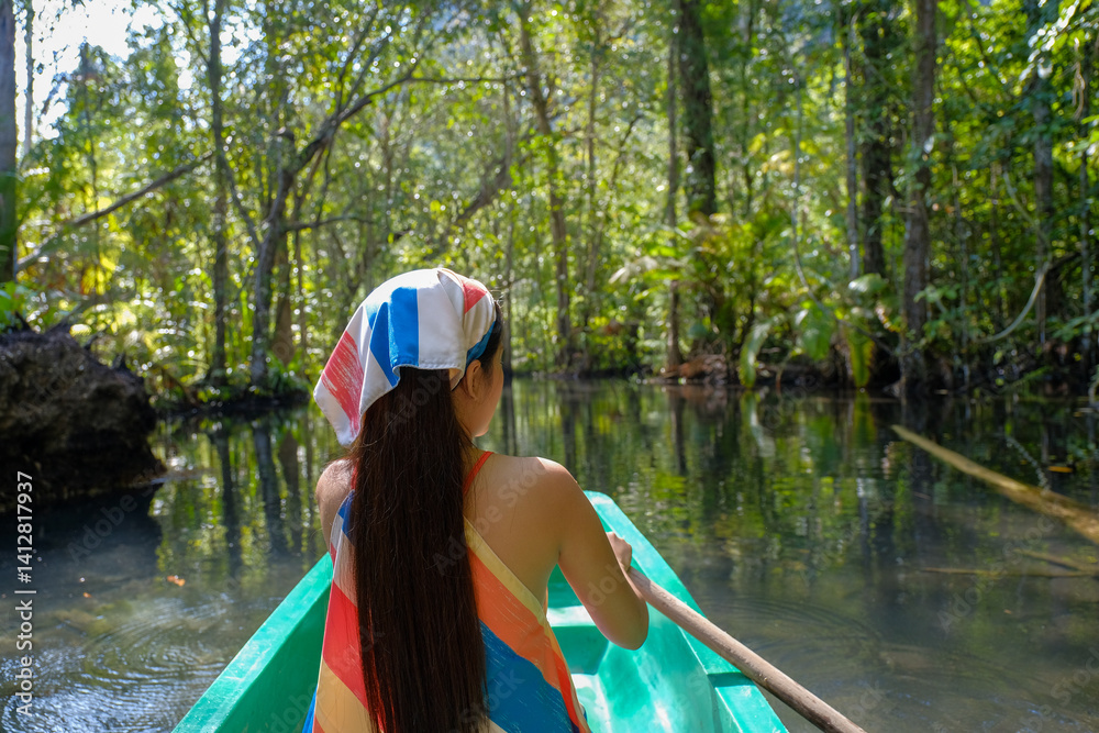 woman paddles green canoe through serene forest river, surrounded by lush greenery and sunlight filtering through trees