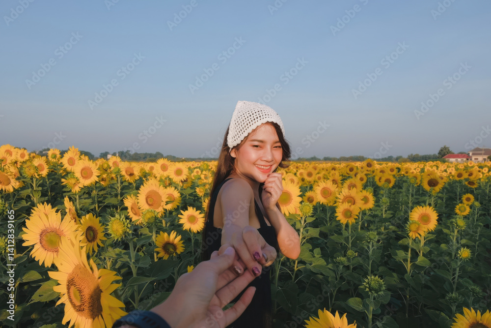 woman in sunflower field smiles while holding someone hand, wearing white knit hat and black dress