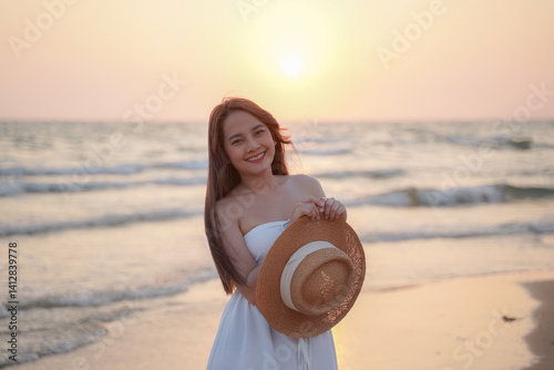 Obraz na płótnie woman in white dress smiles joyfully while holding straw hat on beach at sunset w salonie