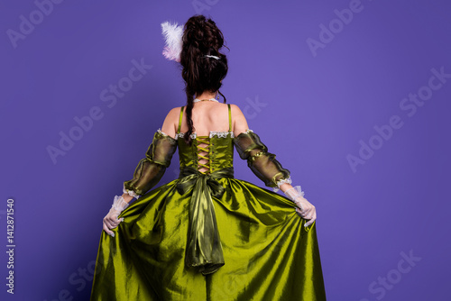 Elegant woman in a vintage-inspired green dress posing against a violet backdrop, showcasing baroque style and historical charm