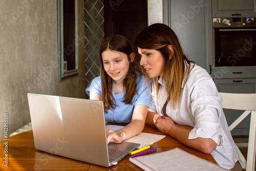 Daughter showing mom something exciting on internet on laptop screen sitting at table in kitchen. Happy parenthood and motherhood. Happy family concept.
