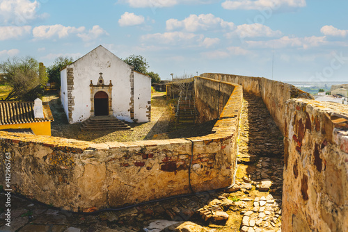 Stone pathway along the Castle of Castro Marims wall leads to a small white chapel within the fortress grounds.