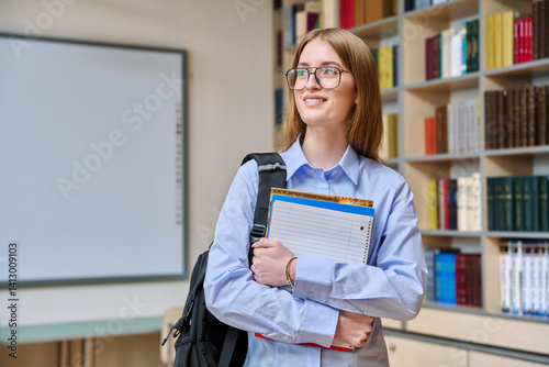 Portrait of student teenager girl holding textbooks inside classroom library