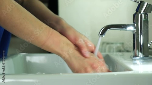 A girl in a blue medical suit washes hands. It soap with soap and carefully cleanses under the dda under the tap. Covid, Epivate. High quality FullHD footage