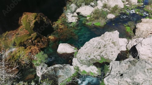 Cascading waterfall flowing over jagged rocks, surrounded by lush greenery, embodying raw wilderness beauty in untouched natural environment