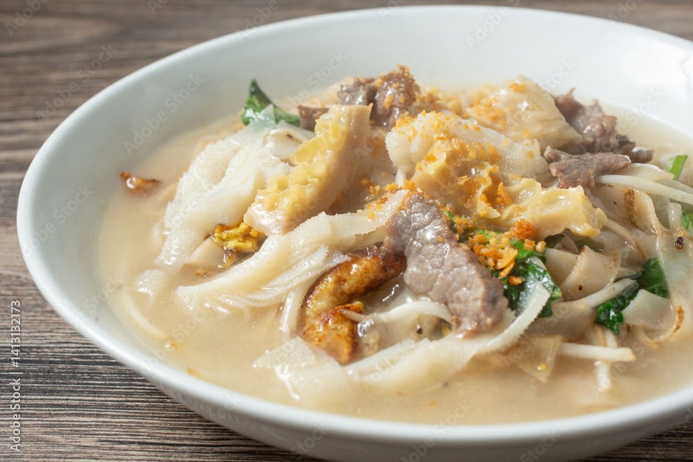 A closeup view of a bowl of tripe and rice noodles in gravy.
