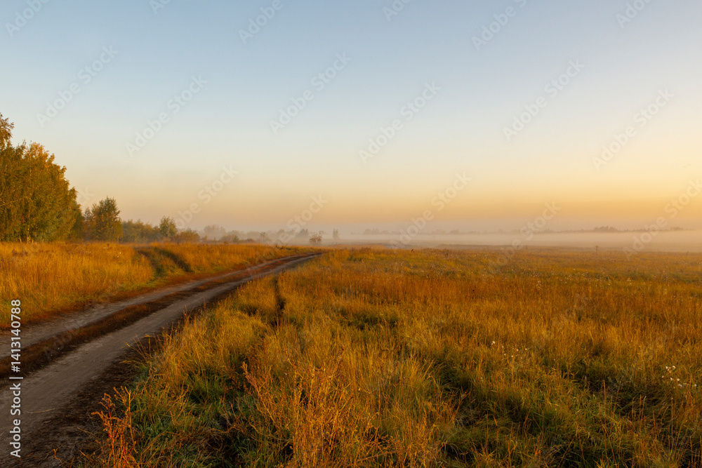 Fototapeta premium Picturesque view of landscape against sky in foggy weather. Warm autumn morning. Picturesque view of road in field against sky during sunrise