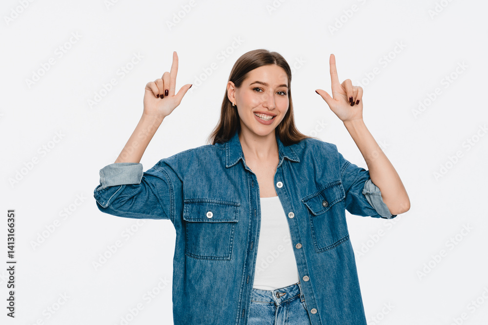 Wow top promo. Excited brunette girl in casual denim smiling and pointing fingers up, showing special advertisement, checking out banner and looking amazed at camera, white background. Wow top promo. Excited brunette girl in casual denim smiling and pointing fingers up, showing special advertisement, checking out banner and looking amazed at camera, white background.